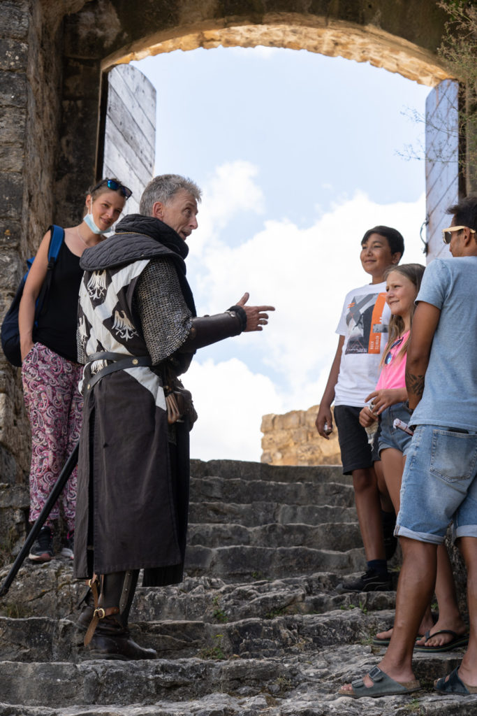 Messire Pons, un membre fondateur de la compagnie des Faydits d'Oc, discute avec des visiteurs lors de leur représentation au château de Peyrelade. Rivière-sur-Tarn, août 2020.