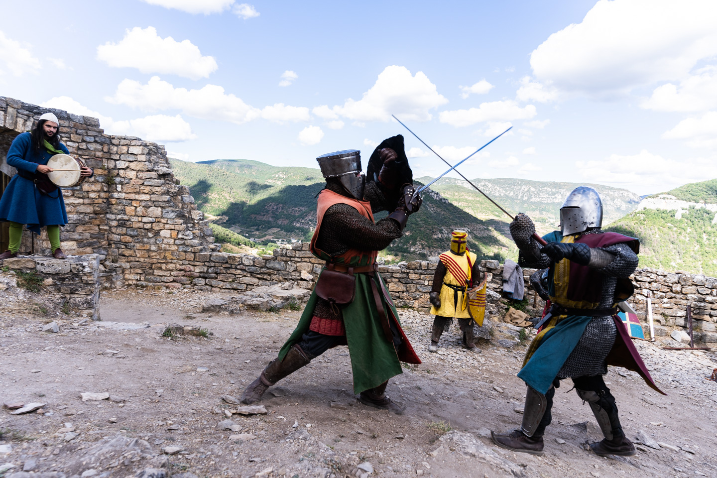 Des membres de la compagnie médiévale "Les Faydits d'Oc" en tenue de chevaliers croisent le fer pendant une représentation au château de Peyrelade sous les regars d'un troubadour et d'un troisième chevalier. Rivière-sur-Tarn, août 2020.