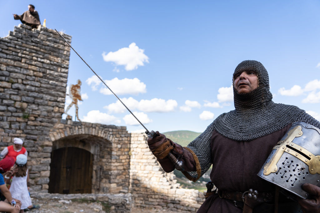 Sire Yvan, de la compagnie médiévale "Les Faydits d'Oc", brandit sont épée le casque à la main pendant une représentation au château de Peyrelade. Rivière-sur-Tarn, août 2020.