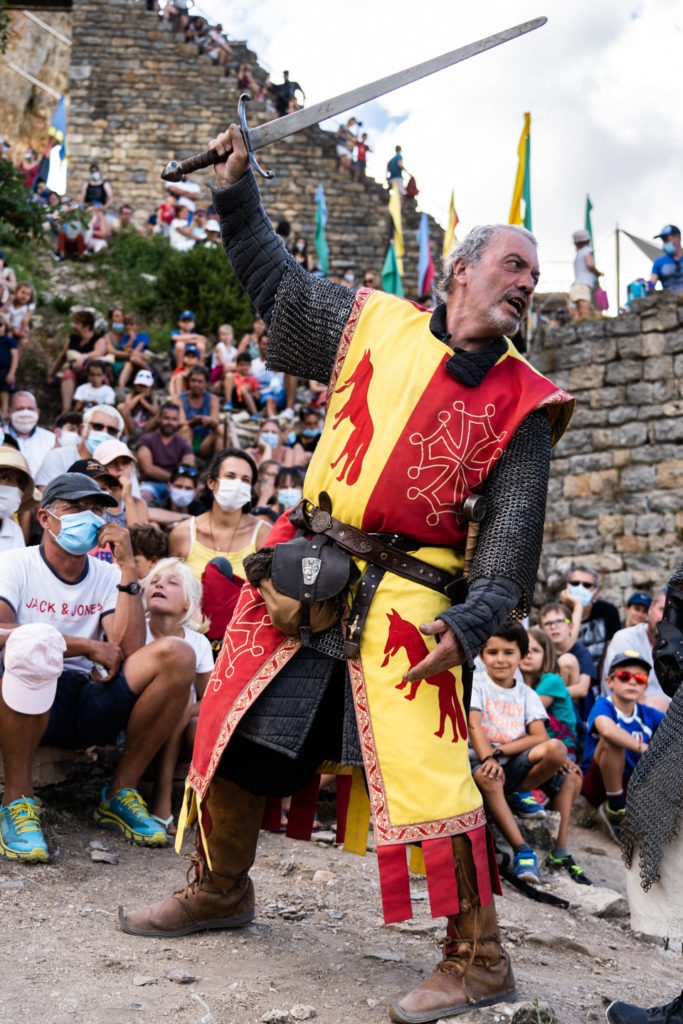 Messire Roger, de la compagnie médiévale "Les Faydits d'Oc", démontre le maniement de l'épée pendant une représentation devant un parterre de spectateurs au château de Peyrelades. Les touristes portent un masque en raison de la situation sanitaire liée au Covid-19. Rivière-sur-Tarn, août 2020.