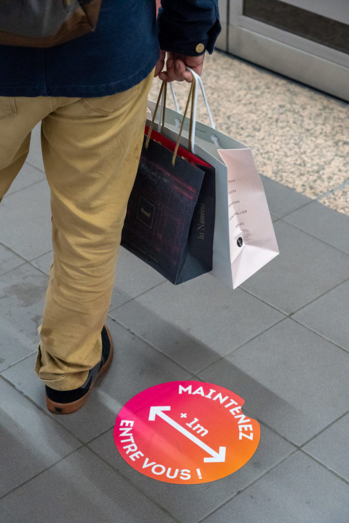 Plan rapproché sur un usager du métro ayant fait ses courses de Noël. Il est debout sur le quai, à côté d'une étiquette prônant la distanciation physique dans le cadre des mesures barrières contre la Covid-19. Toulouse, le 21 décembre 2020.