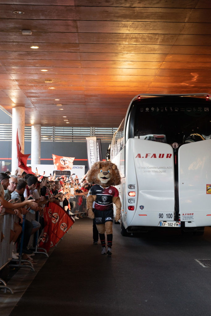 Ovalion, la mascotte du Stade Toulousain, détourne l'attention des spectateurs alors que le bus des joueurs toulonnais arrive au stade. Après une année de matches à huis-clos en raison de la crise sanitaire, le public a pu de nouveau se rendre au stade Ernest Wallon à l’occasion du match de clôture de la 2e journée du Top 14. Champion de France en titre, le Stade Toulousain recevait le Rugby Club Toulonnais. Le match s'est joué à guichets fermés et près de 19000 contrôles de pass sanitaires ont été effectués à l'entrée du stade. Le Stade Toulousain l’a remporté par 41 à 10. Toulouse, stade Ernest Wallon, le 12 septembre 2021.