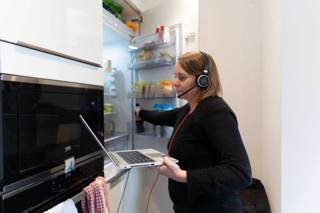 Son ordinateur à la main et son casque sur les oreilles, une employée en télétravail prend une boisson dans son réfrigérateur juste avant le début d'une vidéoconférence avec ses collègues. Toulouse, 26 novembre 2020.