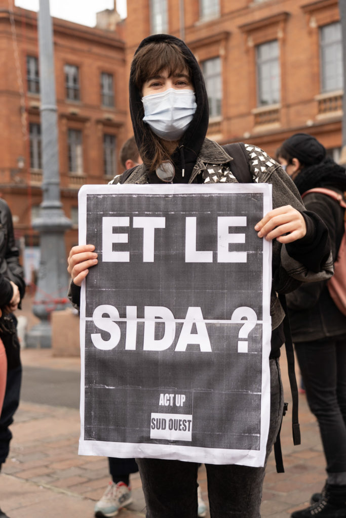 Louise Lourdon tient une pancarte ("Et le Sida?") dénonçant la politique sanitaire du gouvernement à l'occasion du rassemblement organisé par ActUp Sud-Ouest pour la journée mondiale contre le VIH/SIDA.  Elle dénonce notamment la politique sanitaire du gouvernement pendant la crise du Covid. Ancienne présidente d'Act Up Sud-Ouest, Louise Lourdon a été condamnée en première instance à 300€ d'amende avec sursis "pour infjures publiques" suite à une plainte de la Manif Pour Tous concernant une contre-manifestation ayant eu lieu en 2017. Elle a fait appel de ce jugement et le tribunal de grande instance de Toulouse rendra sa décision le 8 décembre. Toulouse, le 1er décembre 2020.