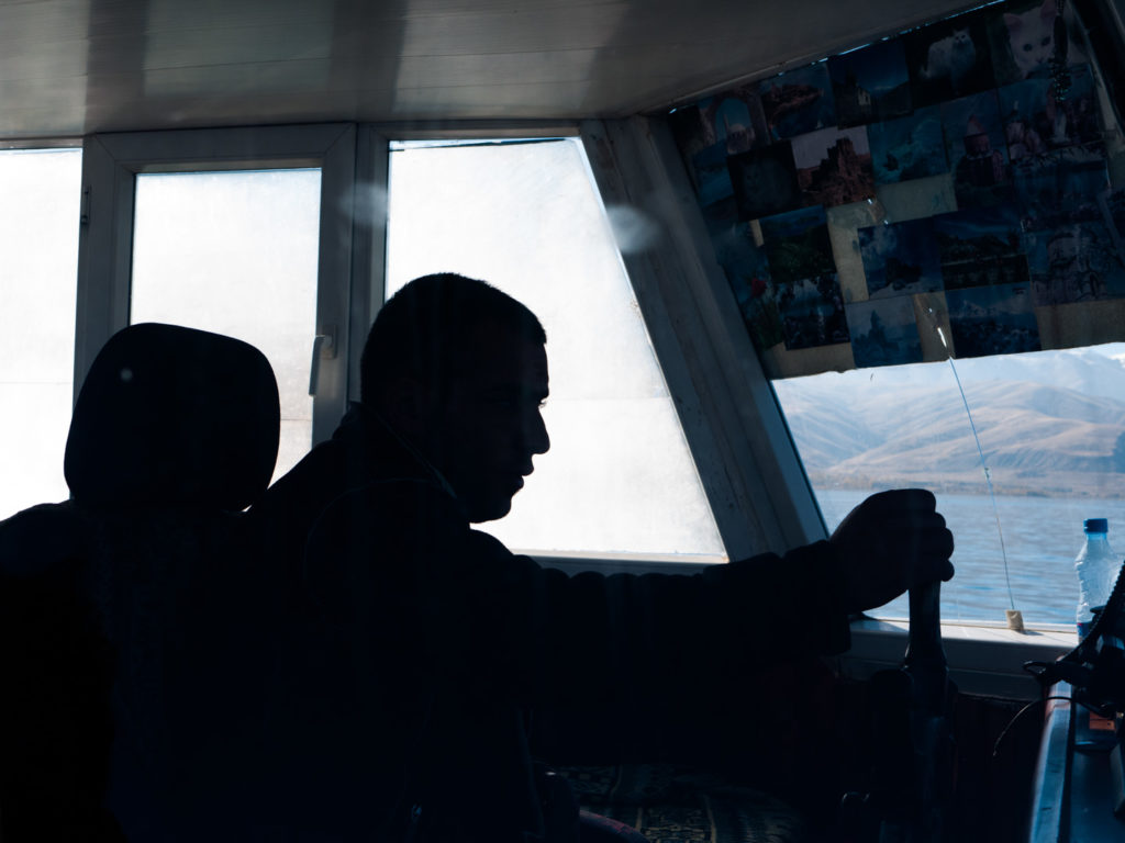 Silhouette du barreur opérant le bateau menant à l'île d'Akdamar dans le lac de Van. Sur le pare-brise, des photos et cartes postales typiques de la région. Van (Turquie), novembre 2010.